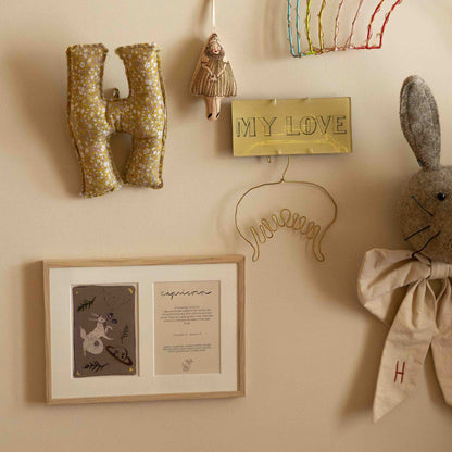 Ingelijste dubbele Hazel &amp; George Steenbok-poster aan de wand tussen kinderkamerdecoratie, met een gevlochten letter H-kussen, een pluche konijn en een gouden &