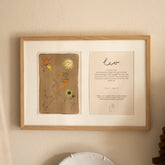 Ingelijste dubbele Hazel & George Leeuw-poster aan de wand in een lichte houten lijst