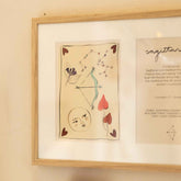Close-up van de linkerkant van de ingelijste dubbele Hazel & George Boogschutter-poster met de illustratie van pijl en boog en een maangezicht
