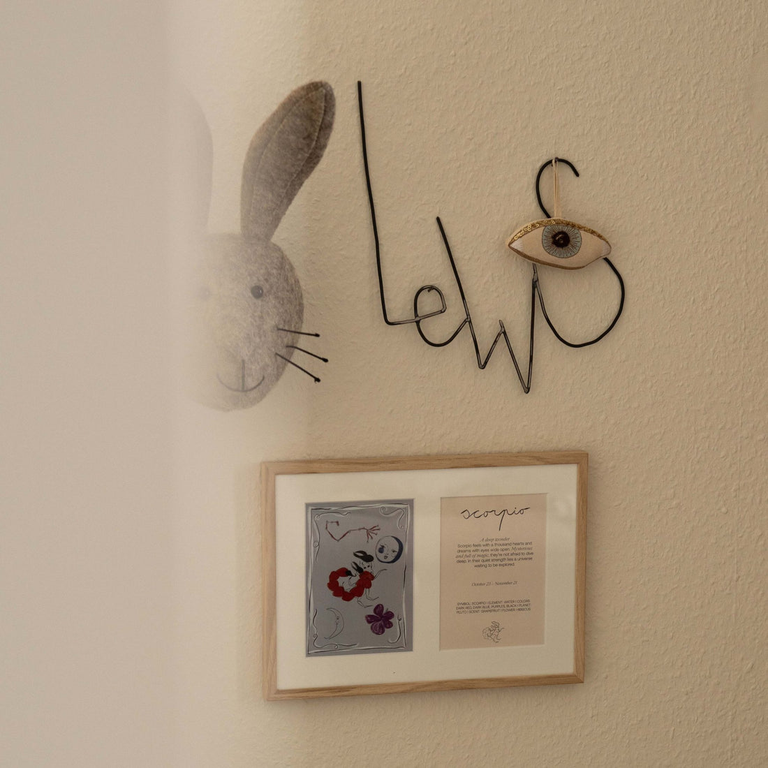 Ingelijste dubbele Hazel &amp; George Schorpioen-poster aan de wand, naast een naamdecoratie van metaaldraad en een knuffelkonijnenkop