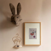 Ingelijste Hazel & George Schorpioen-poster aan de wand, naast een knuffelkonijnenkop en een hangende oog-decoratie