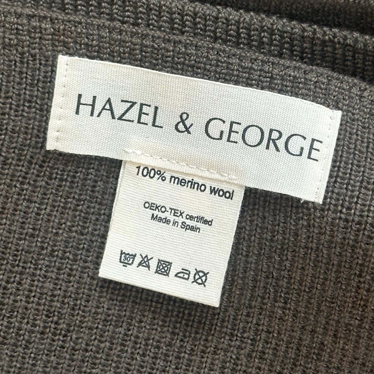 Close-up of the Hazel &amp; George label reading 100% merino wool, OEKO-TEX certified, Made in Spain, on a Merino Blanket in Mosswood