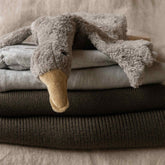 Stack of folded Hazel & George Merino Blankets in Mosswood, styled with a plush swan toy