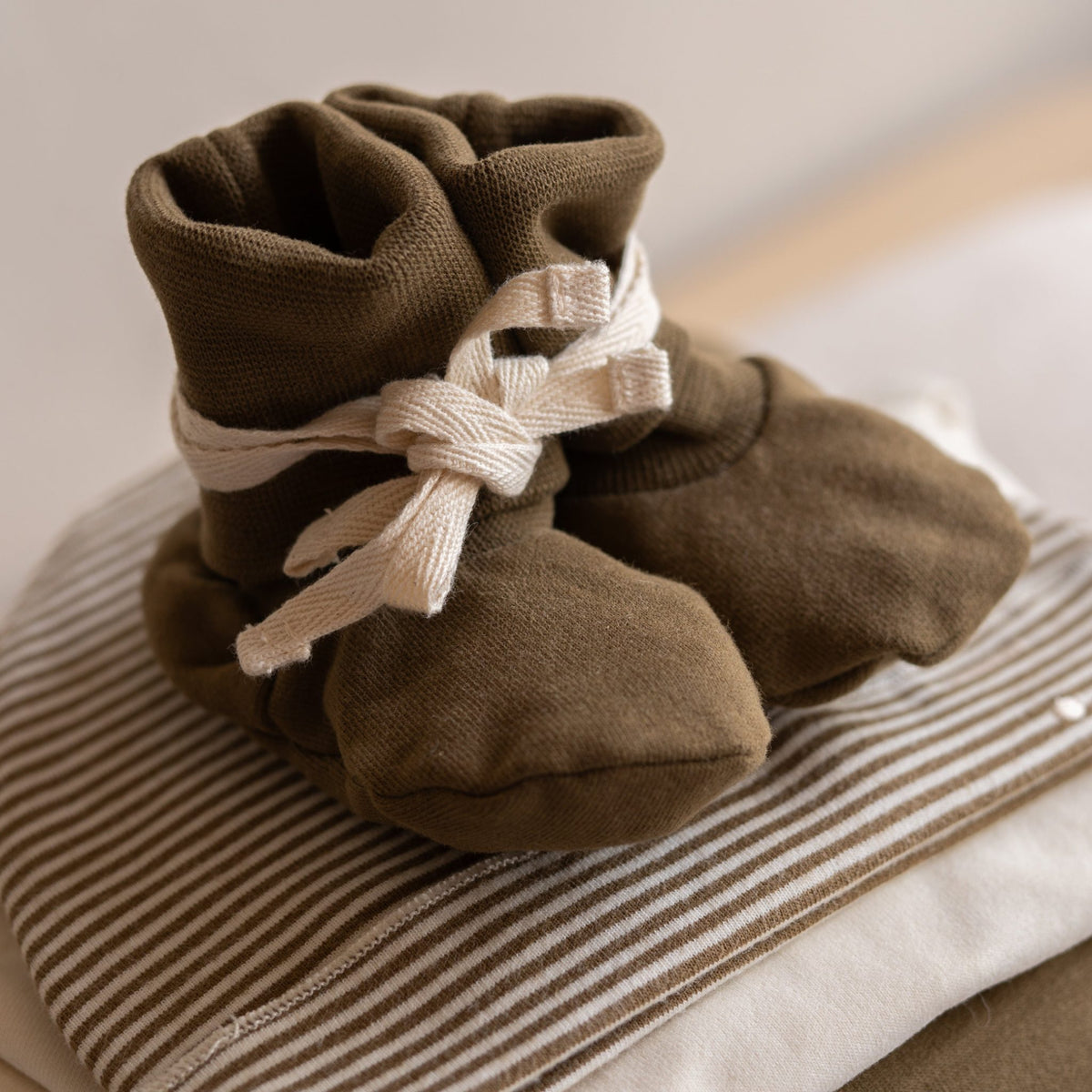 Gray Label Ribbed Baby Booties in Woody, styled on top of folded striped baby clothing