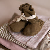 Close-up of the Gray Label Ribbed Baby Booties in Woody, styled on top of folded striped baby clothing