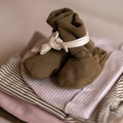 Close-up of the Gray Label Ribbed Baby Booties in Woody, styled on top of folded striped baby clothing