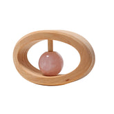 A wooden rattle with a pink rose quartz attached to its center, forming an oval shape.