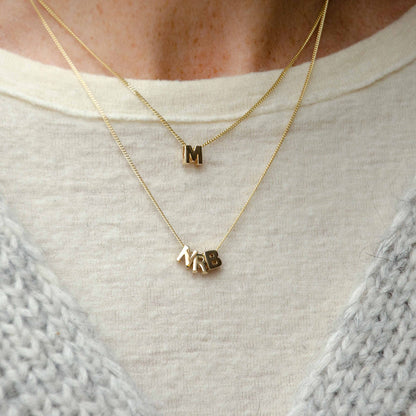 Hazel &amp; George Chunky Initial 14K Gold, layered gold necklaces worn on a sweater with chunky letter charms spelling M and NRB