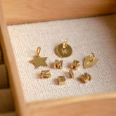 Hazel & George Chunky Initial 14K Gold, assortment of gold charms in a jewelry box, including a star, a round disc, a heart and chunky bubble letters