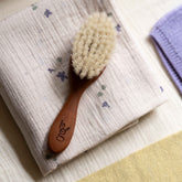 Hazel & George wooden baby hair brush lying on a violet-print muslin swaddle blanket