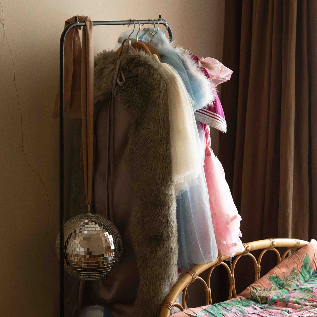 Hazel &amp; George Dazzling Disco Ball Large hanging from a clothing rail with dress-up costumes, next to a rattan bed frame