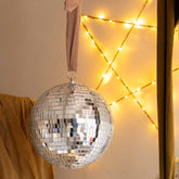Close-up of the Hazel & George Dazzling Disco Ball Large in front of a fairy-light star, next to a mustard bed canopy