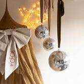 Hazel & George Dazzling Disco Balls in different sizes hanging next to a fairy-light star and the Festive Bow on a mustard bed canopy