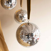 Close-up of three Hazel & George Dazzling Disco Balls in graduated sizes hanging from mustard ribbons, showing the mirrored mosaic tiles