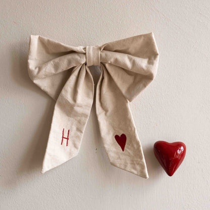 Hazel &amp; George Canvas Festive Bow Small on a wall, embroidered with the initial H and a red heart, next to a red heart-shaped knob