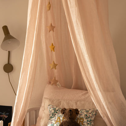 Hazel &amp; George Linen Bed Canopy in Craie hanging over a bed with a star garland inside, a floral &