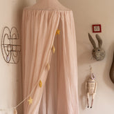 Hazel & George Linen Bed Canopy in Craie in a nursery, with a star garland hanging inside, a felt rabbit head and decorative wall pieces