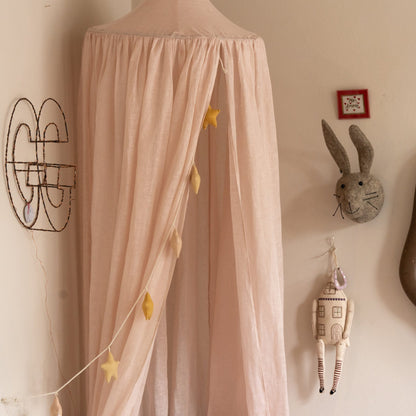 Hazel &amp; George Linen Bed Canopy in Craie in a nursery, with a star garland hanging inside, a felt rabbit head and decorative wall pieces