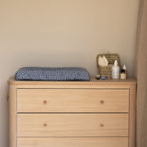 Hazel & George Linen Changing Mat Cover in Vichy on a wooden dresser in a nursery, with a basket and baby care products nearby