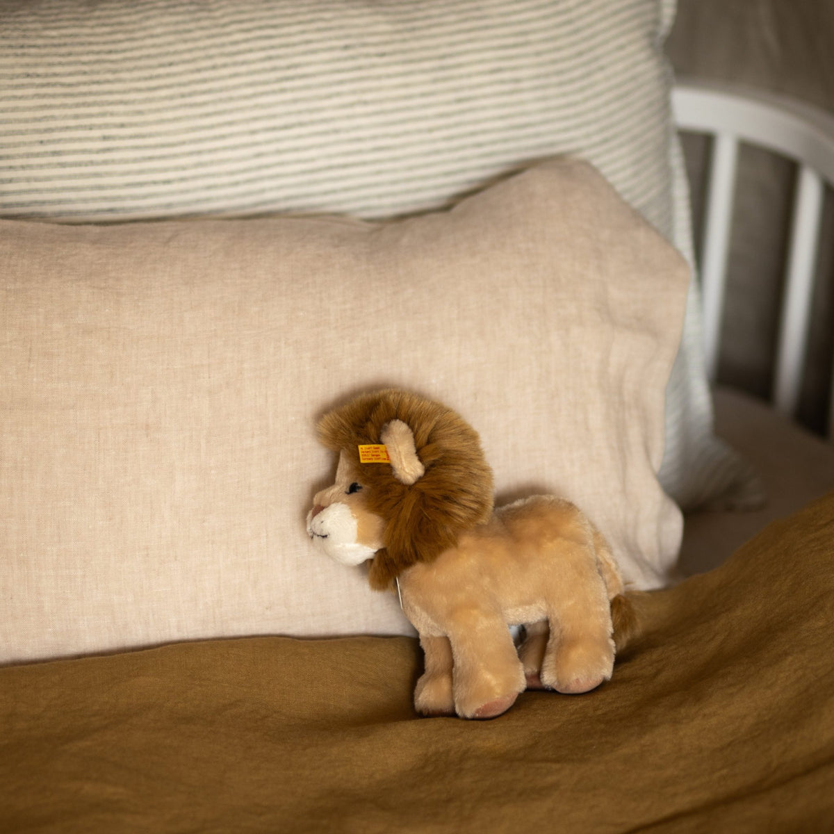 Nursery crib styled with a Hazel &amp; George linen cushion in Naturel, a striped pillow, and a plush lion toy