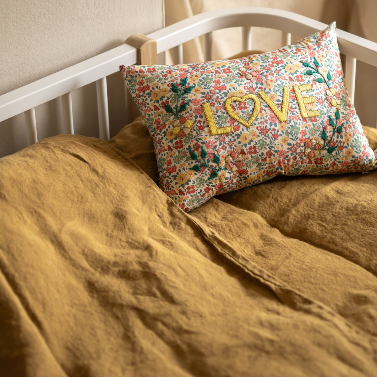 Hazel &amp; George Linen Duvet Cover in Dore on a toddler bed with a bed rail, styled with a floral cushion