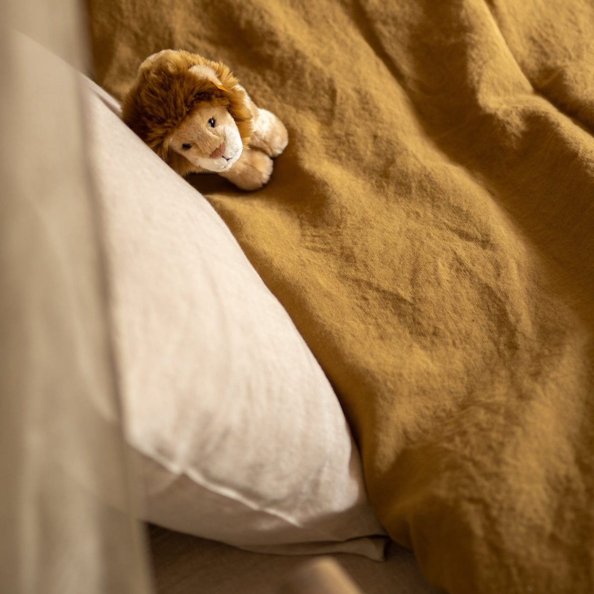 Hazel &amp; George Linen Duvet Cover in Dore on a bed, with a stuffed lion toy