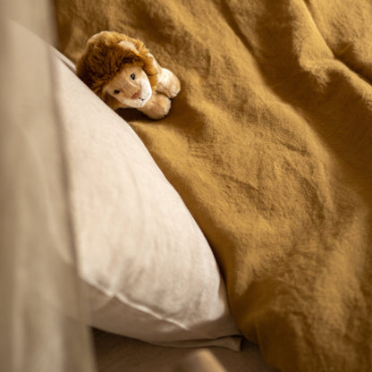 Hazel &amp; George Linen Duvet Cover in Dore on a bed, with a stuffed lion toy