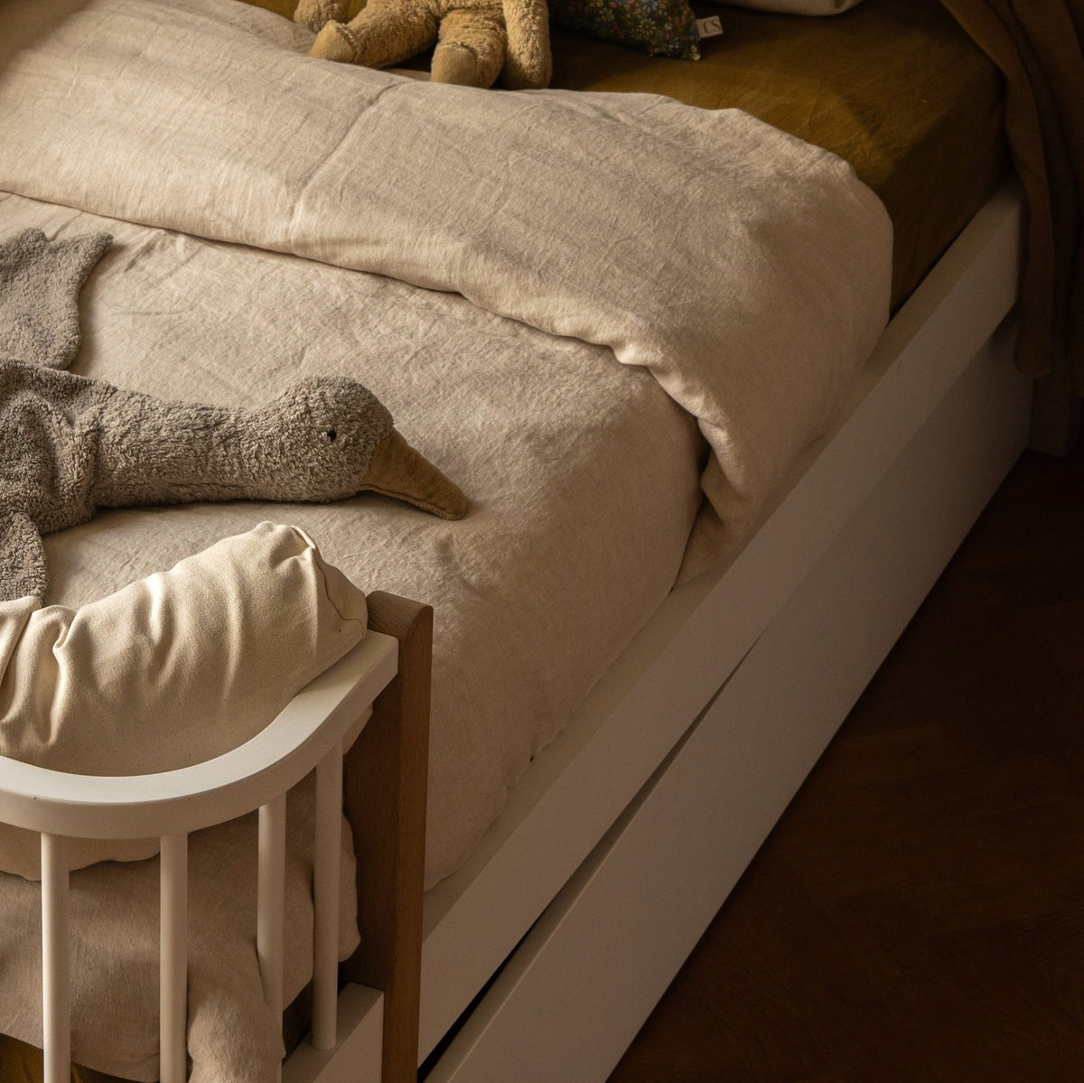 Hazel &amp; George Linen Duvet Cover in Naturel on a toddler bed with a bed rail, with a stuffed goose toy