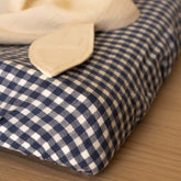 Close-up of the elastic corner of the Hazel & George Fitted Sheet in Vichy, with a natural muslin cloth folded on top