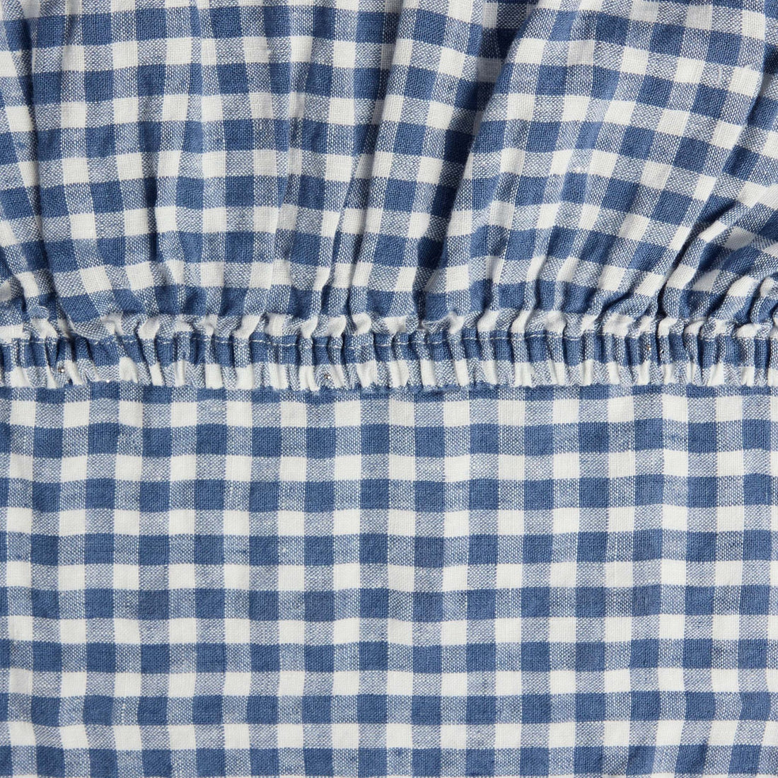 Close-up of the elastic corner of the Hazel &amp; George Fitted Sheet in Vichy, showing the woven blue-and-white check pattern