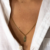 Hazel & George Rectangular Initial Hanger 14K Gold, gold necklace with a rectangular pendant engraved with the letters AMH worn on the chest with a white shirt