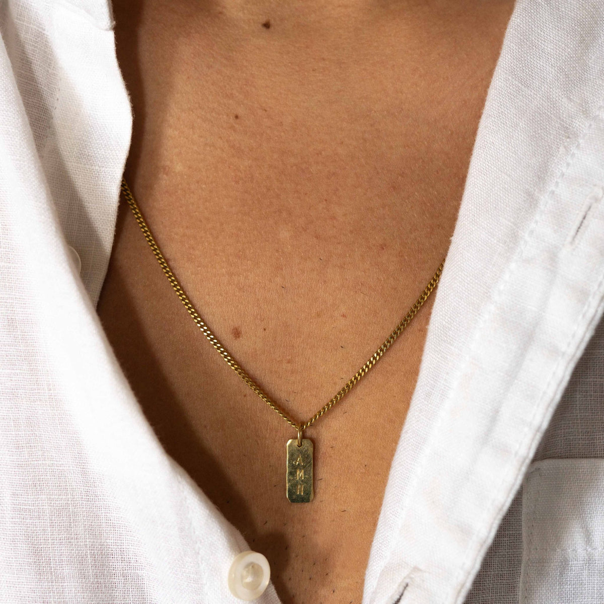 Hazel &amp; George Rectangular Initial Hanger 14K Gold, gold necklace with a rectangular pendant engraved with the letters AMH worn on the chest with a white shirt