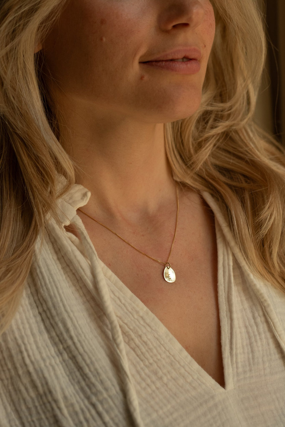 Hazel &amp; George Necklace 14K Gold with large initial hanger E, worn by a woman in a cream linen blouse