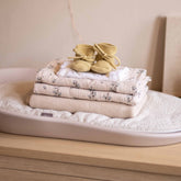 Hvid Baby Booties Light Yellow displayed on a stack of folded baby textiles on a changing pad, lifestyle photo