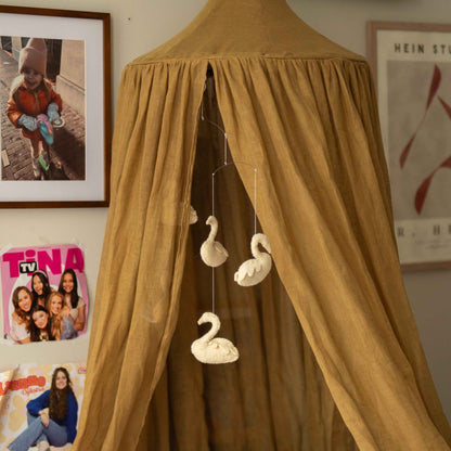 Hazel &amp; George Linen Bed Canopy in Dore in a teenage bedroom, with a felt swan garland hanging inside and photos and posters on the wall