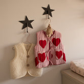 Two Hazel & George Metal Star Hooks mounted on a nursery wall, holding a cream teddy vest and a pink heart-print vest