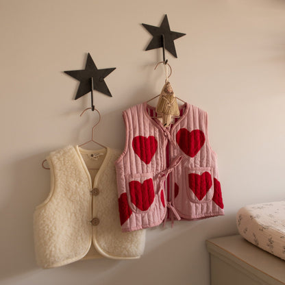 Two Hazel &amp; George Metal Star Hooks mounted on a nursery wall, holding a cream teddy vest and a pink heart-print vest