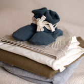 Gray Label Ribbed Baby Booties in Blue Grey, styled on top of folded baby clothing