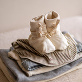 Gray Label Ribbed Baby Booties in Cream, styled on top of folded striped baby clothing