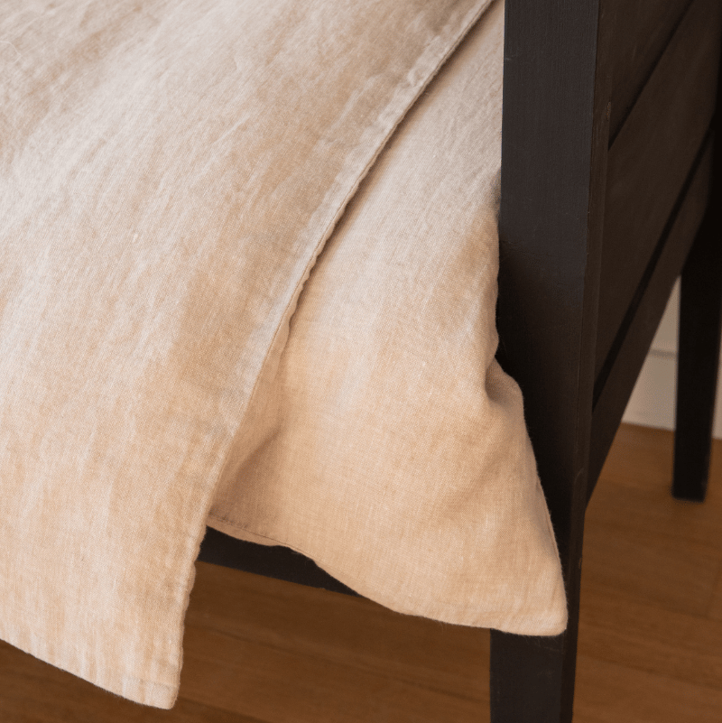 Close-up of the Hazel &amp; George Linen Duvet Cover in Naturel draping over a dark wooden bed frame